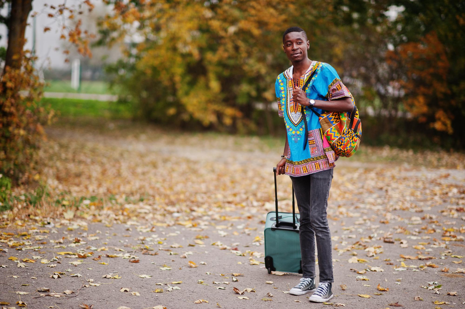 african-man-in-africa-traditional-shirt-on-autumn-park-with-backpack-and-suitcase-emigrant-traveler
